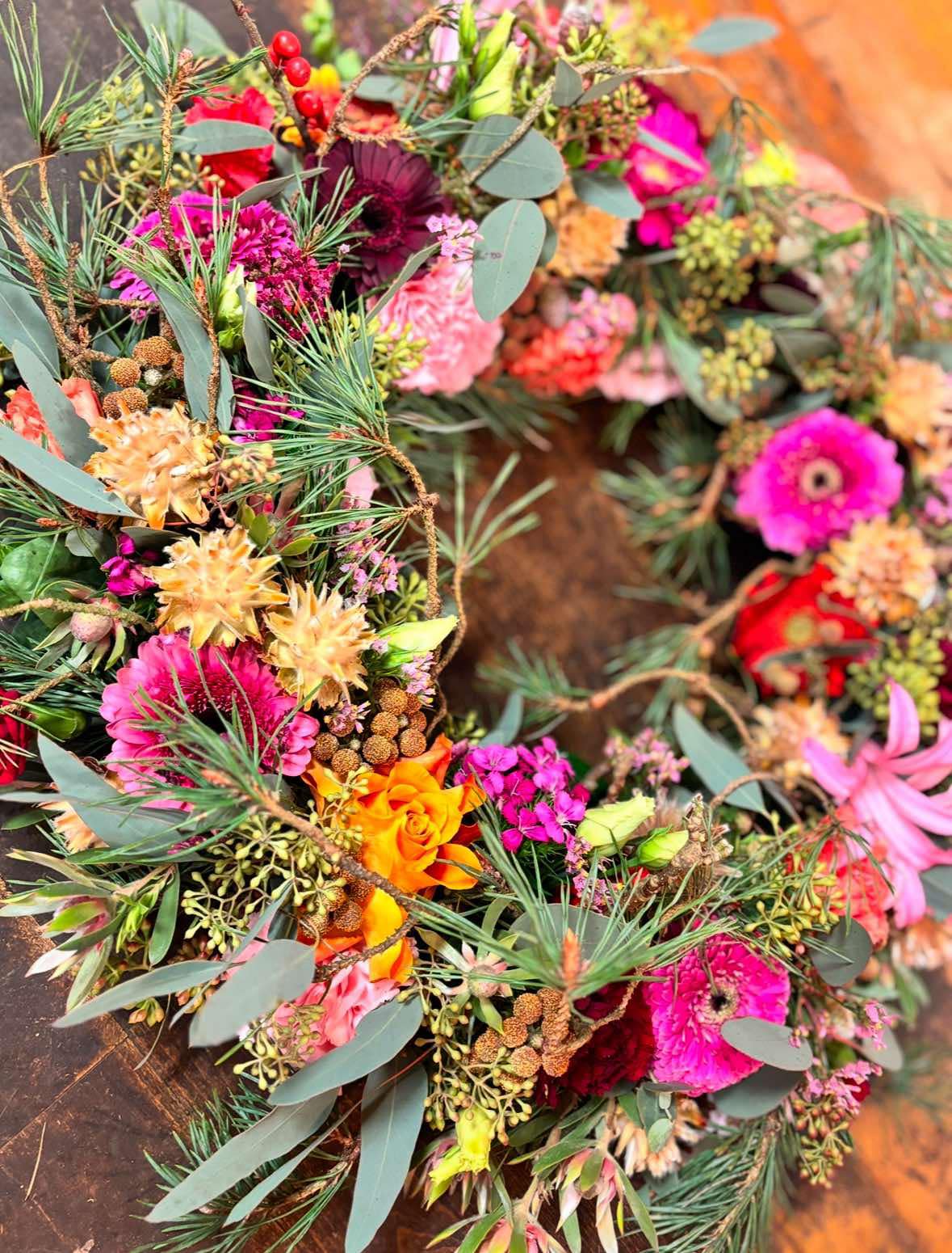 Vinterkrans med farverige blomster, fyrnålegran og kogler. 