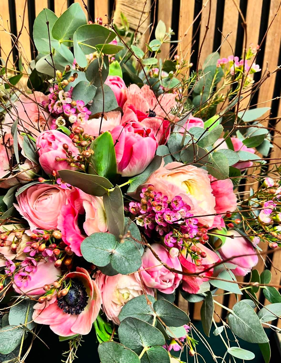 Tæt og sprudlende buket bundet med ranunkler og tulipaner i rosa nuancer. 