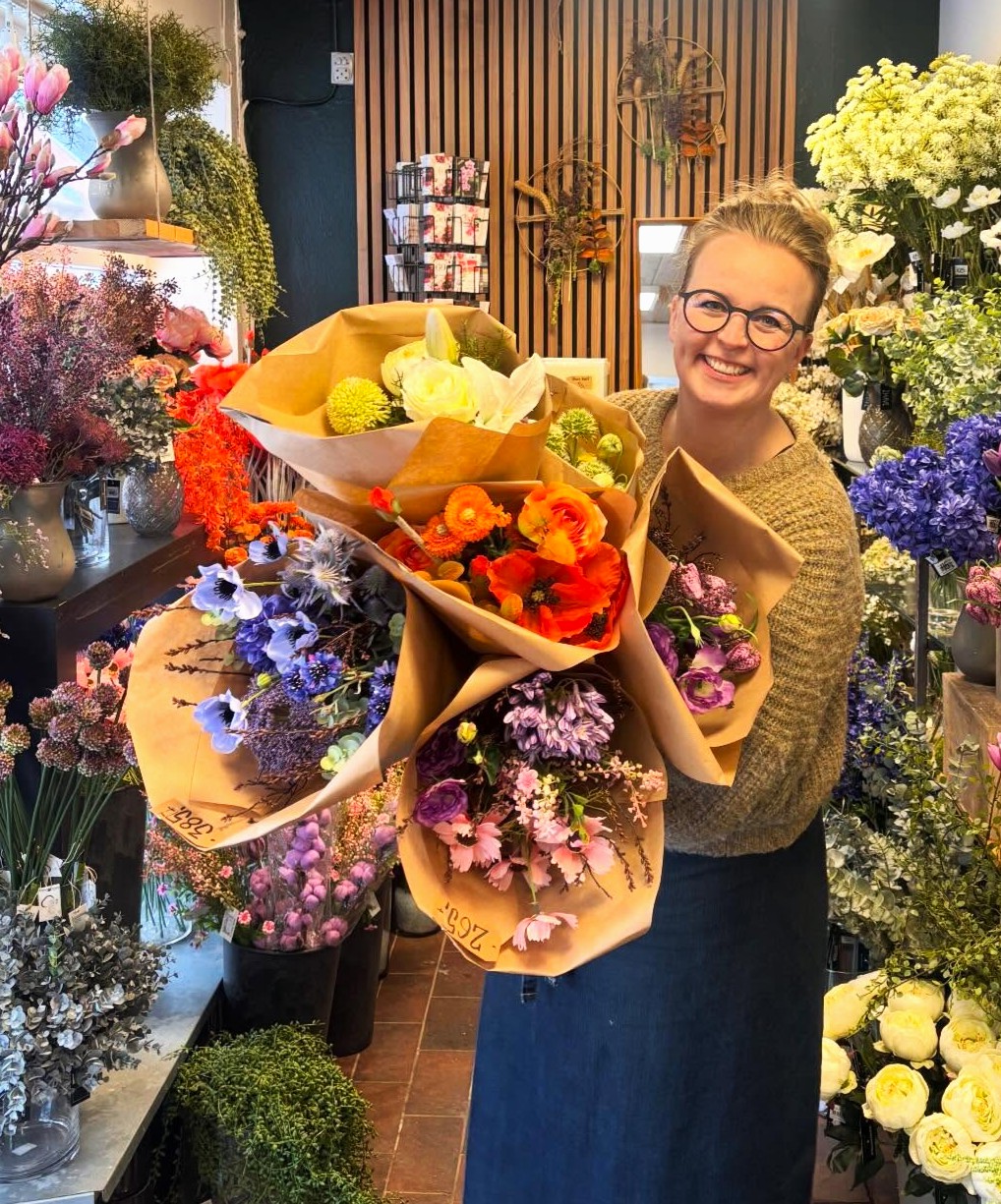 Indehaver Tina Dam står smilende med buketter i farverige nuancer i armene. 