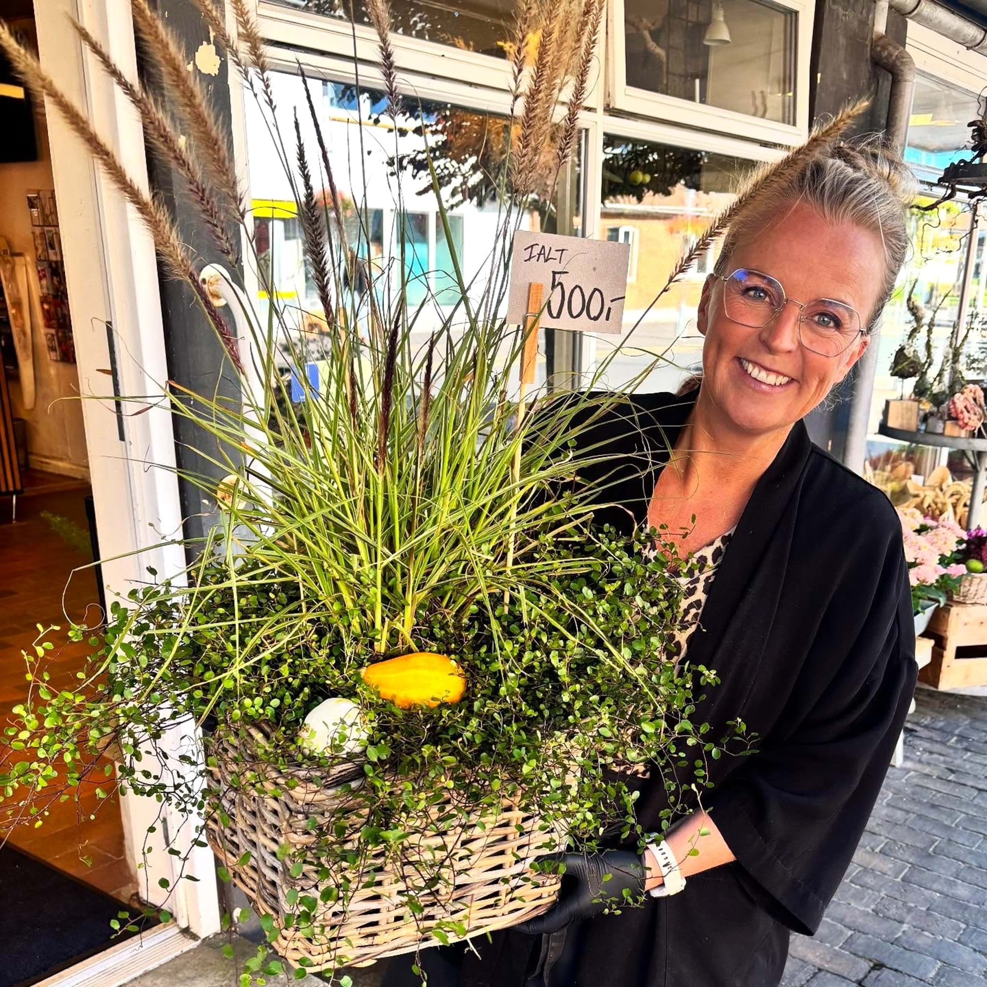 Indehaver Tina Dam holder en fletkurv der er plantet med pampas, pletter i luften og græskar i bunden.