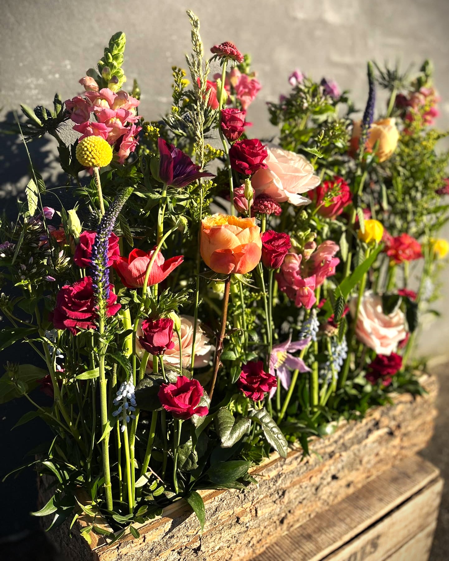 Kasse stukket med forårets blomster i varme og røde farver. 