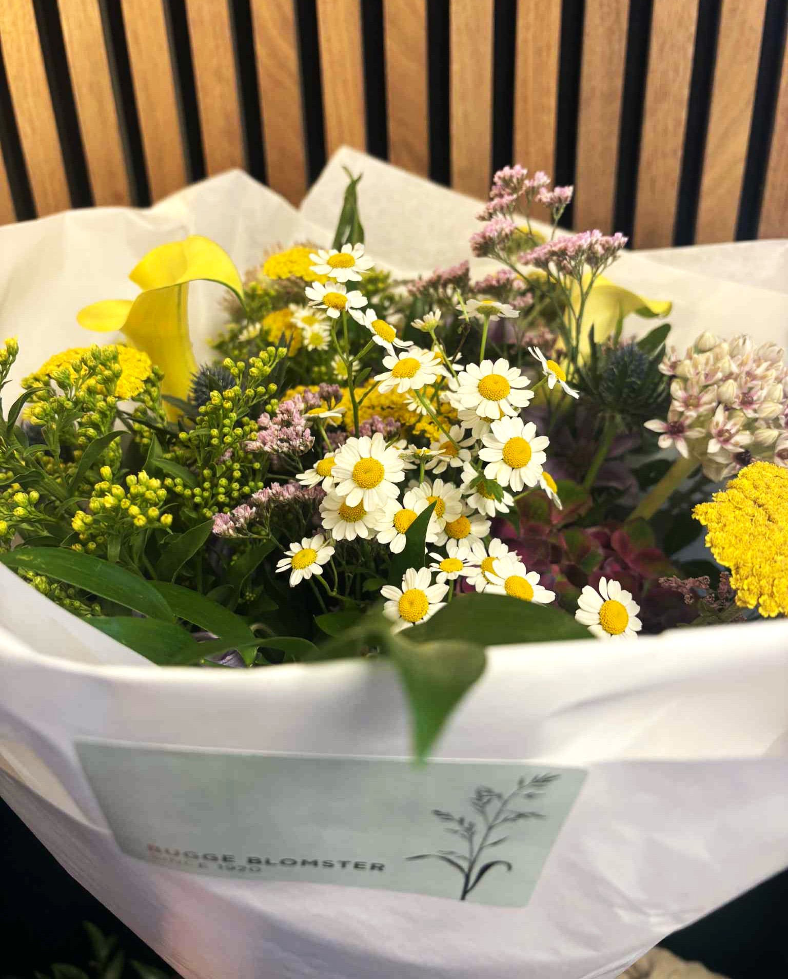 Naturlig og landlig buket bundet med et vildt udtryk og indeholder blomster i gule, lyserøde og grønne nuancer. 