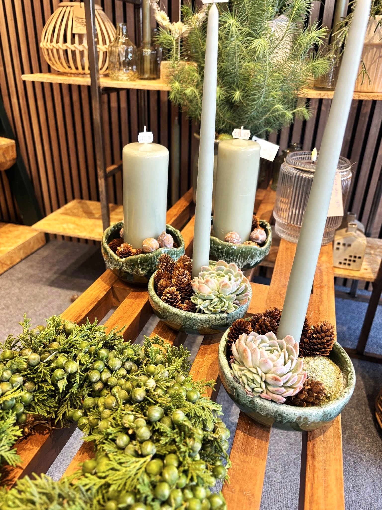 Krans af grene og grønne bær, samt fade med husløg og lys, står på en trællebænk. 